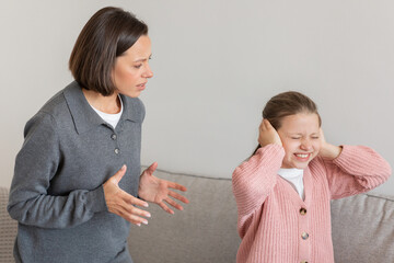 Wall Mural - Strict sad millennial caucasian woman scolding teenage daughter, covering ears with hands, freaking out