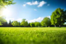Blurred Background Image Of Spring Nature With A Neatly Trimmed Lawn Surrounded By Trees Against A Blue Sky With Clouds On A Bright Sunny Day.