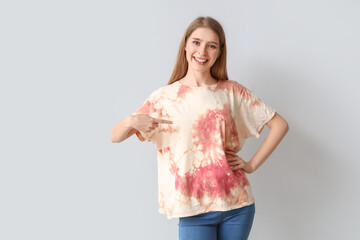 Wall Mural - Young woman pointing at tie-dye t-shirt on light background