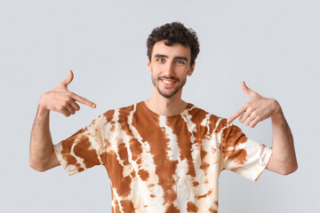 Wall Mural - Handsome man pointing at tie-dye t-shirt on light background