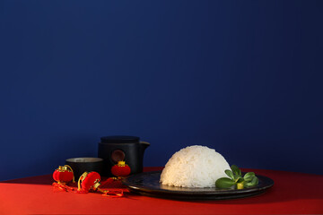 Plate with tasty Chinese rice, tea set and lanterns on color background