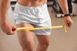 Athletic man measuring thigh with tape in gym, closeup