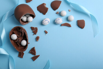 Wall Mural - Tasty broken chocolate eggs with different sweets on light blue background, flat lay. Space for text