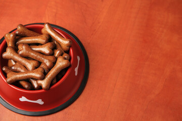 Wall Mural - Red bowl with bone shaped dog cookies on wooden table, space for text