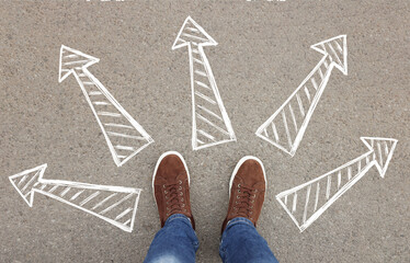 Wall Mural - Choosing future profession. Man standing in front of drawn signs on asphalt, top view. Arrows pointing in different directions symbolizing diversity of opportunities