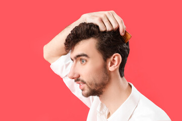 Poster - Young brunette man combing hair on red background, closeup