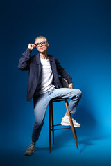 Poster - Young tattooed man in eyeglasses sitting on blue background