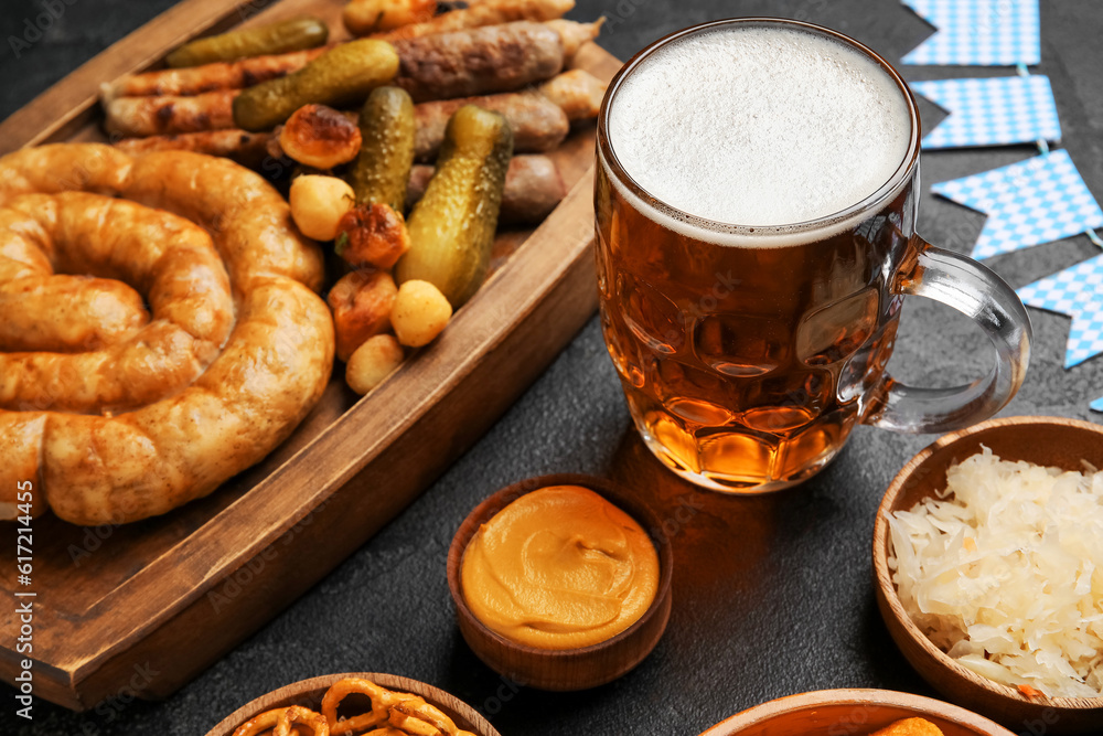 Mug of cold beer and different snacks on black background. Oktoberfest celebration
