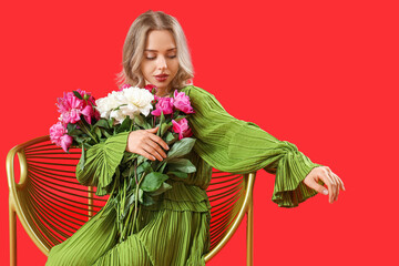 Wall Mural - Young woman with beautiful peony flowers in armchair on red background