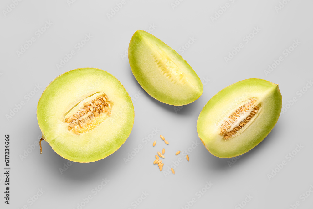 Half of sweet melon with pieces and seeds on grey background