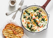Baked shakshuka with spinach, tomatoes and mozzarella in a cast-iron pan and grilled ciabatta on a light background, top view