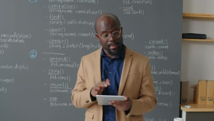 tracking shot of male african american teacher going there and back in front of blackboard giving le
