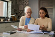 © AnnaStills - Grandmother and granddaughter sitting by table in the kitchen and discussing financial bills while one of them explaining information