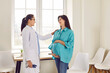Doctor supporting pregnant woman. Pregnant lady visits doctor at clinic. Friendly, smiling obstetrician in white medical coat puts hand on shoulder of young pregnant girl. Pregnancy healthcare concept