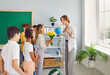 © Studio Romantic - Grateful little children boys and girls on Teacher Appreciation Day give flowers to woman tutor congratulating on professional holiday stand in classroom of school. Elementary education for schoolkids