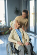 © AnnaStills - Happy grandmother with disability and granddaughter looking at one another in living room while senior woman sitting in wheelchair