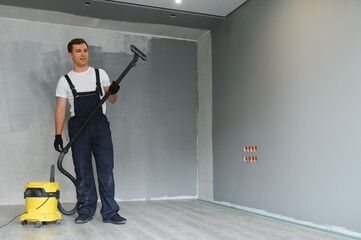 A worker using a vacuum cleaner removes construction debris. A worker is cleaning industrial premises. apartment after repair using polysos