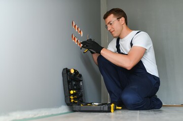 Wall Mural - Electrician in uniform mounting electric sockets on the white wall indoors