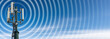 © Alberto Masnovo - Closeup of a telecommunications tower with antennas (aerial) and radio waves, against a clear blue sky with clouds and copy space.