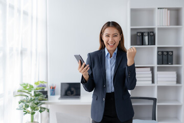 Happy asian businesswoman raising hands with victory smiling happily with smart phone. The concept of success at work