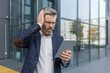 © Liubomir - Mature gray haired boss businessman received message with bad news, man shocked by bankruptcy and upset reading message from outside office building, holding tablet.