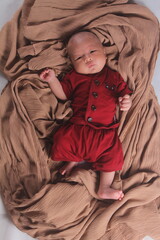 Portrait of a two month old boy looking at camera cutely and smiling as he sleeps in brown clothes in newborn baby photo shoot
