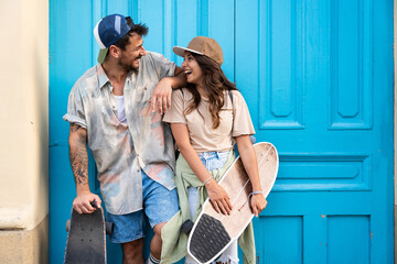 Tourists couple skateboarders riding skates. Happy young travelers longboarding together on sunset on pavement. Stylish man and woman in trendy outfit skating outdoors in touristic destination streets