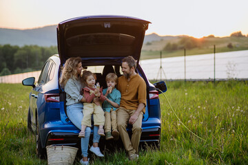 Happy family sitting in a car trunk and waiting for charging.