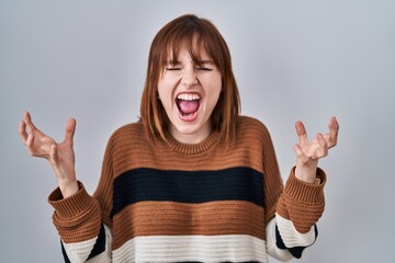 Wall Mural - Young beautiful woman wearing striped sweater over isolated background celebrating mad and crazy for success with arms raised and closed eyes screaming excited. winner concept