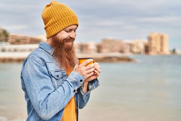 Canvas Print - Young redhead man smiling confident drinking cup of coffee at seaside