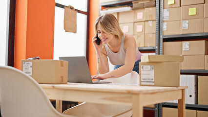 Poster - Young blonde woman ecommerce business worker using laptop talking on smartphone at office