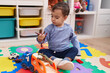 © Krakenimages.com - Adorable hispanic boy playing with car and dinosaur toy sitting on floor at kindergarten