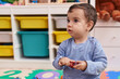 © Krakenimages.com - Adorable hispanic boy playing with dinosaur toy sitting on floor at kindergarten