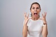 Beautiful brunette woman standing over isolated background crazy and mad shouting and yelling with aggressive expression and arms raised. frustration concept.