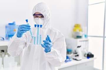 Wall Mural - Young blonde woman scientist wearing security uniform holding test tubes at laboratory