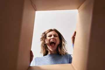 Sticker - Beautiful woman opening cardboard box angry and mad screaming frustrated and furious, shouting with anger. rage and aggressive concept.