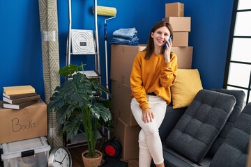 Canvas Print - Young blonde woman talking on smartphone sitting on sofa at new home