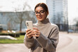 © Andrei - Beautiful woman student in eyeglasses using a phone in the street. Safe and happy