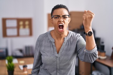 Canvas Print - African american woman working at the office wearing glasses angry and mad raising fist frustrated and furious while shouting with anger. rage and aggressive concept.