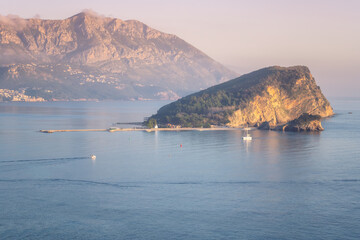 Amazing view of the water area of the beautiful city of Budva with the island of St. Nicholas surrounded by the calm waters of the Adriatic Sea in the golden hour before sunset, Montenegro