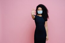 Ethnic Woman With Curly Hair, Making Stop Gesture, Says No To COVID-19. Wearing Mask, Black Dress, Virus Protection.