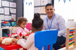 © Krakenimages.com - Hispanic man and girls playing supermarket game sitting on table at kindergarten