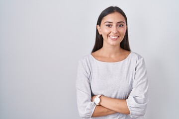 Wall Mural - Young hispanic woman standing over white background happy face smiling with crossed arms looking at the camera. positive person.