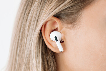 White wireless headphone for sports, running, cycling, walking in the ear of a young caucasian blonde woman listening to music. Close up