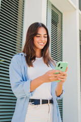 vertical portrait of smiling young woman using mobile phone app , texting, playing game, shopping on