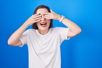 Canvas Print - Middle age hispanic woman standing over blue background covering eyes with hands smiling cheerful and funny. blind concept.