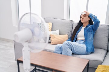 Canvas Print - Young chinese woman using ventilator sitting on sofa at home