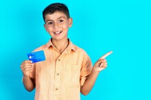 Smiling Little Hispanic Boy Wearing Orange Shirt Showing Debit Card Pointing Finger Empty Space
