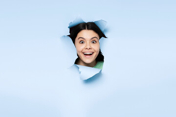 Wall Mural - Beautiful latin teenage girl looking at camera over torn blue background. Young female