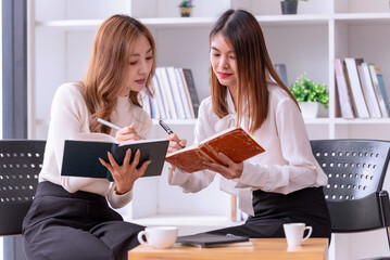  Two young Asian businesswomen discussing a new Idea Presentation business project In Modern Office.